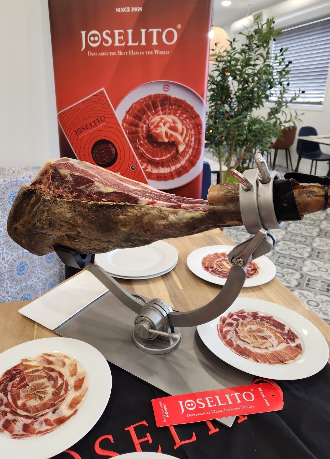 Whole Joselito ham leg on a carving stand surrounded by plates of thinly sliced jamón.