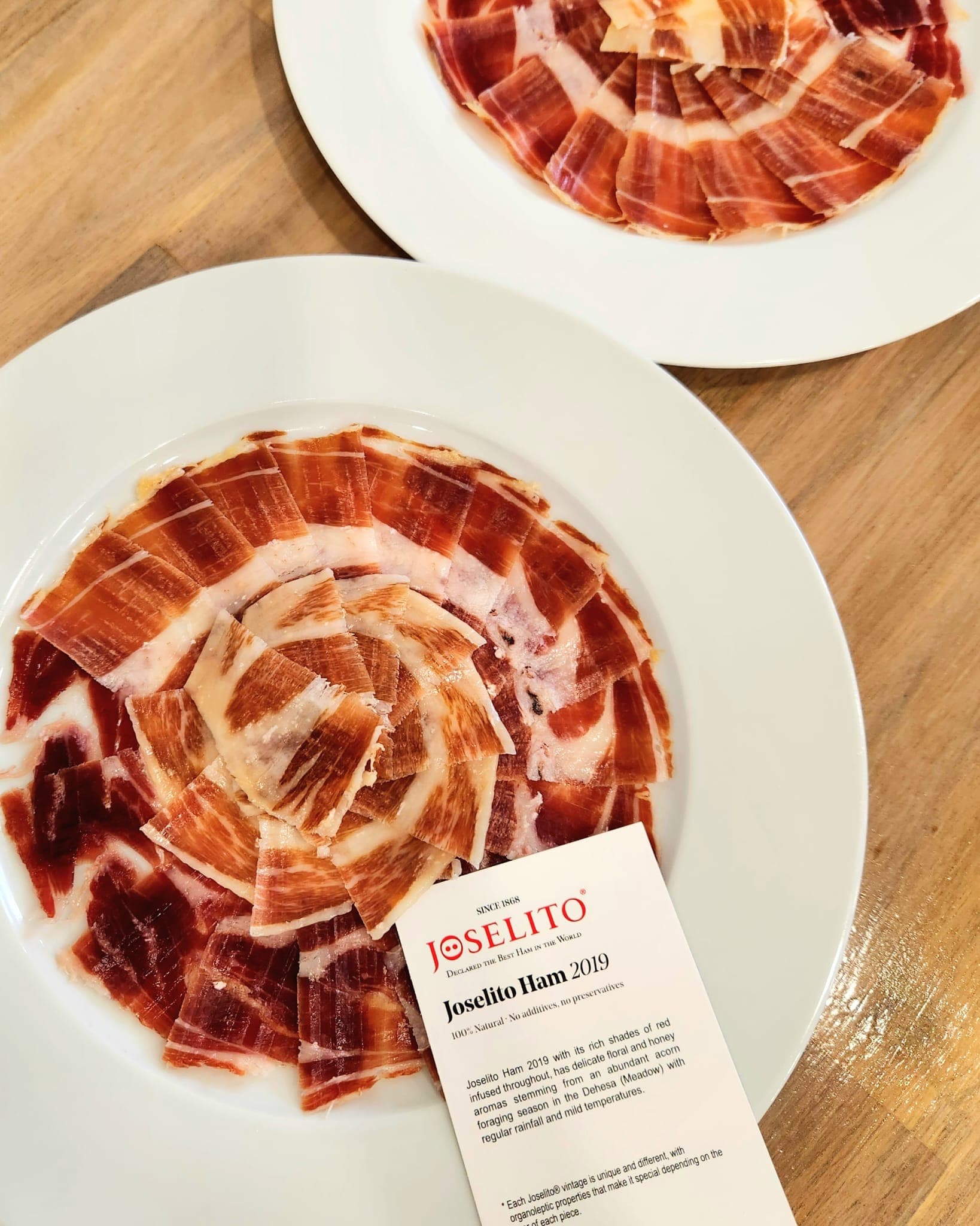 Thinly sliced, marbled Joselito ham arranged in a circular pattern on two white plates.