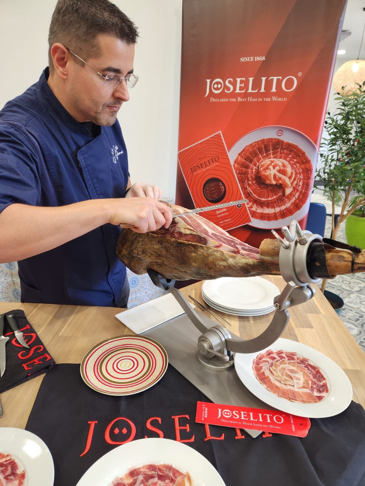 Chef in blue slices thin Joselito Ibérico ham from a cured leg on a stand.